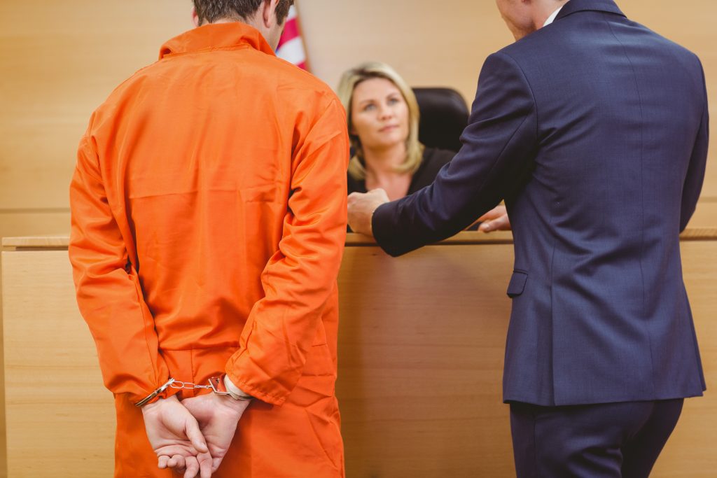 Lawyer and judge speaking next to the criminal in handcuffs - criminal defense attorney