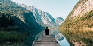 man sitting at the edge of dock on lake